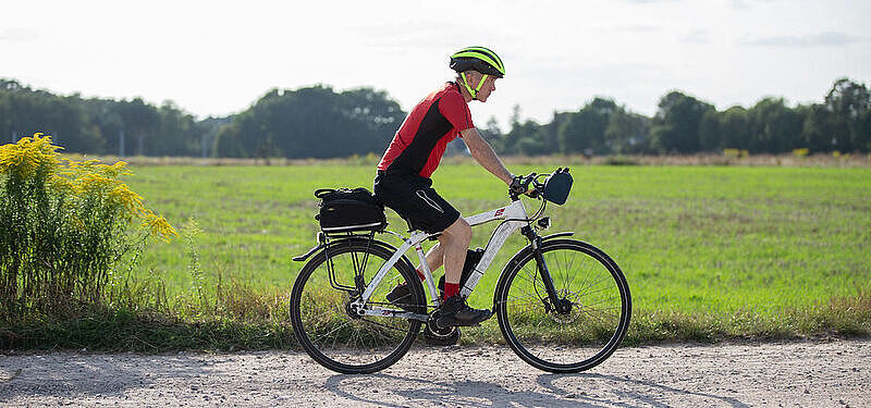 Radfahrer fährt auf einem sportlichen Rad auf einem Radweg vor einer Wieser